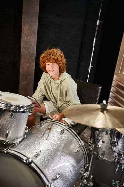 Gai adorable rousse adolescent garçon aux cheveux en tenue confortable tenant téléphone mobile à côté de ses tambours — Photo de stock