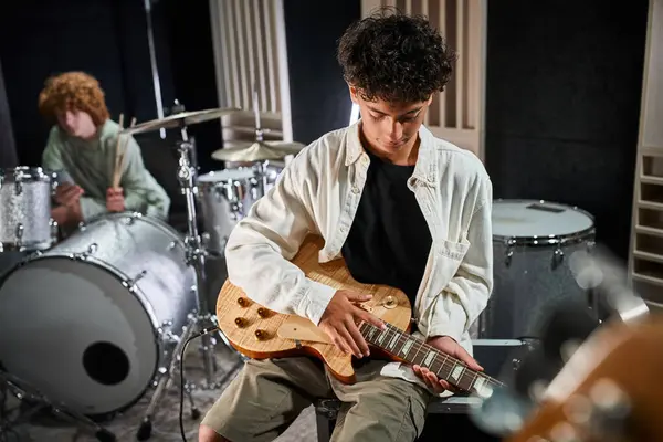 Focus on adorable teenage boy with guitar next to his blurred red haired drummer, musical group — Stock Photo