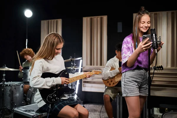 Allegri adorabili adolescenti in abiti casual accoglienti che suonano chitarre e batteria e cantano in studio — Foto stock