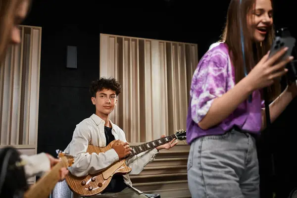 Entzückender netter Teenager, der Gitarre spielt und aufmerksam auf seine Freunde schaut, Musikgruppe — Stockfoto