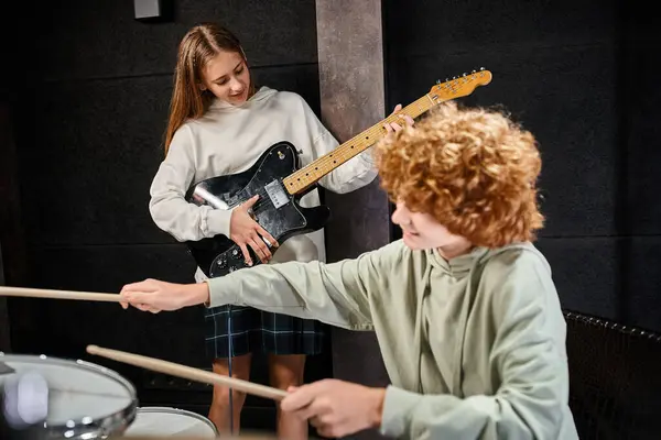 Concentrarsi su allegra bella adolescente che suona la chitarra accanto al suo batterista dai capelli rossi sfocati — Foto stock