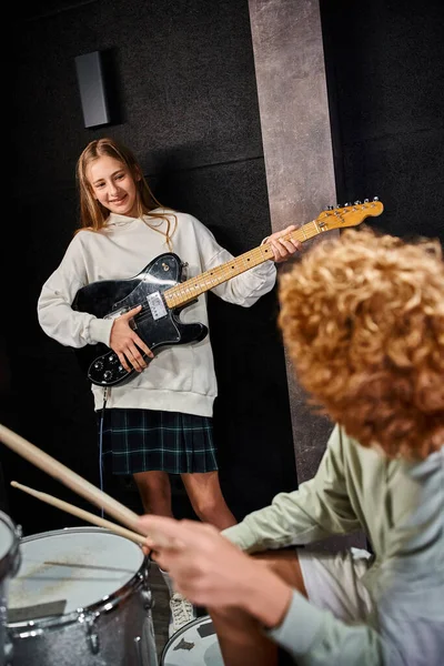Foco em adorável adolescente tocando guitarra e olhando para seu baterista de cabelos ruivos — Fotografia de Stock