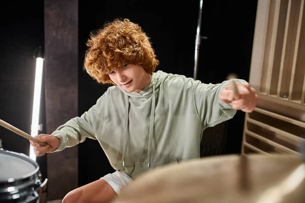 Alegre pelirroja lindo adolescente en cómodo traje tocando su batería activamente mientras en su estudio - foto de stock