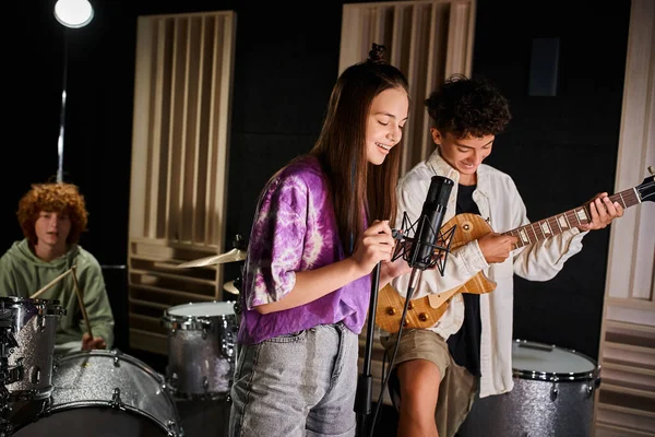 Se concentrar em adolescente alegre menino e menina cantando e tocando guitarra ao lado de seu baterista turvo — Fotografia de Stock
