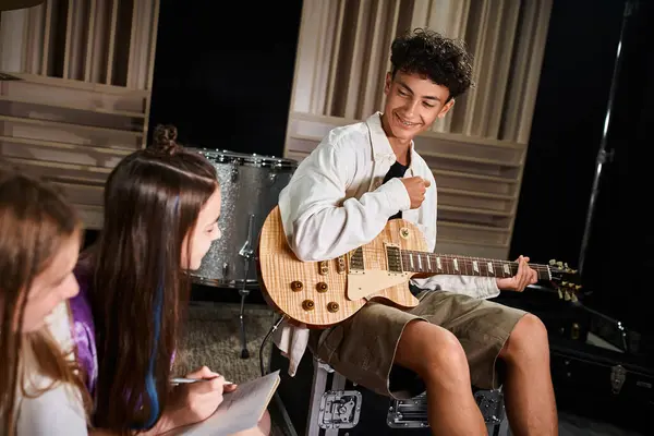 Focus on joyful cute teenage boy with braces holding guitar and looking at his blurred band members — Stock Photo