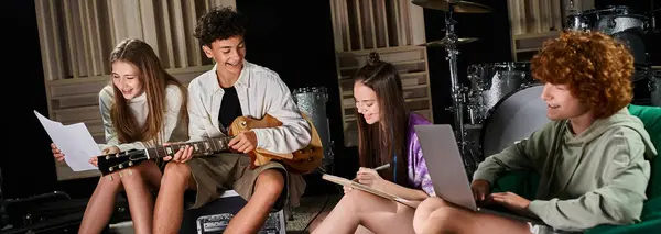 Jolly teenage band members in casual outfits sitting with guitar and laptop writing lyrics, banner — Stock Photo