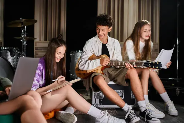 Alegre lindo adolescente banda miembros sentado con la guitarra y el ordenador portátil y escribir letras en el estudio - foto de stock