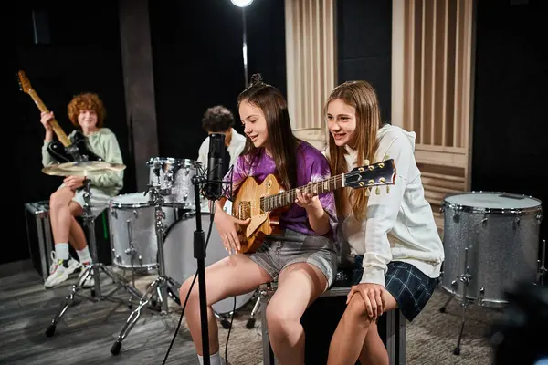 Focus on teenage girls with guitar singing with blurred friends with drums and guitar on backdrop — Stock Photo