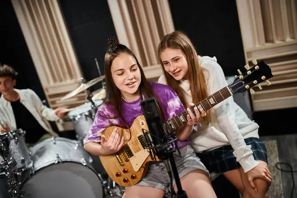 Focus on cheerful talented girls playing guitar and singing with their blurred drummer on backdrop — Stock Photo