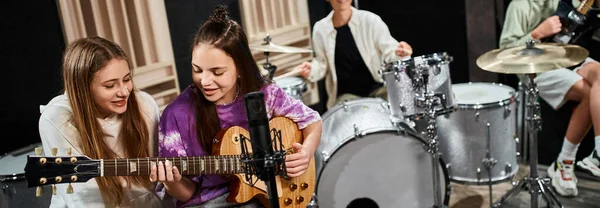 Se concentrar em meninas adolescentes alegres tocando guitarra e cantando perto de seus amigos embaçados, banner — Fotografia de Stock
