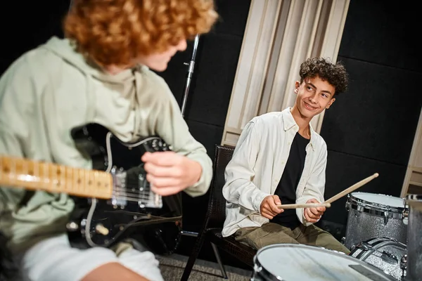 Se centran en el baterista adolescente alegre con frenos sonriendo a su guitarrista de pelo borroso, banda musical - foto de stock