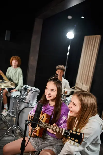 Alegre bonita adolescentes cantando y tocando varios instrumentos en estudio, grupo musical - foto de stock