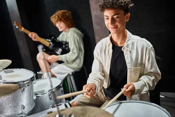 Alegre adorable adolescente con frenos tocando la batería junto a su amigo con la guitarra, grupo musical - foto de stock