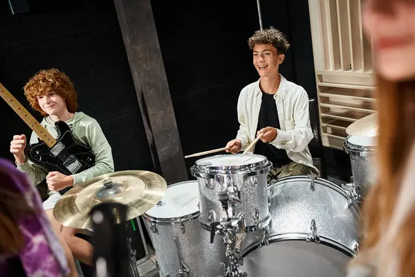 Se concentrar em meninos adolescentes alegres tocando bateria e guitarra ao lado de seus amigos turvos no vocal — Fotografia de Stock