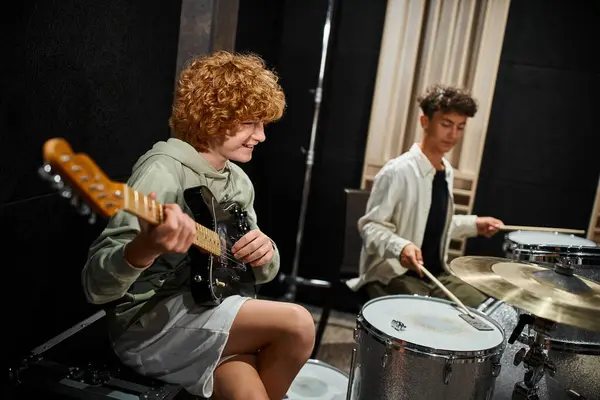 Concentrarsi su allegro ragazzo dai capelli rossi adolescente suonare la chitarra accanto al suo amico offuscata suonare la batteria — Foto stock