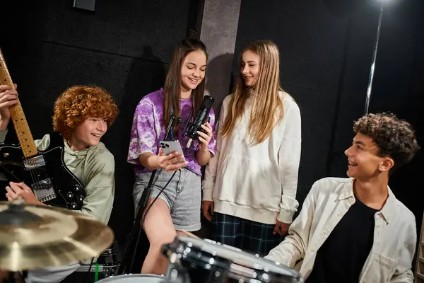 Alegre lindo adolescente niñas cantando y sonriendo mientras niños jugando guitarra y batería en estudio - foto de stock