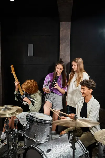 Adorable adolescente chicos jugando instrumentos mientras niñas cantando y mirando el teléfono, grupo musical - foto de stock