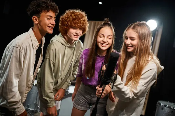 Adolescentes bonitos alegres em trajes vibrantes cotidianos cantando juntos no microfone, grupo musical — Fotografia de Stock