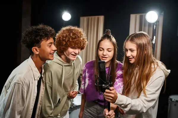 Quatre adolescents joyeux et talentueux en tenue décontractée chantant ensemble en studio, groupe musical — Photo de stock