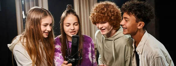 Alegres adolescentes talentosos con atuendos casuales cantando juntos en estudio, grupo musical, pancarta - foto de stock