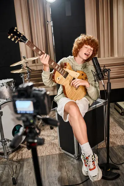Alegre talentoso guitarrista adolescente con atuendo casual tocando instrumento y cantando canción en el estudio - foto de stock