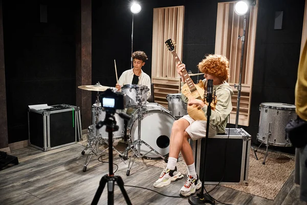 Dos adolescentes talentosos adorables en atuendos vívidos cotidianos tocando la guitarra y la batería en el estudio - foto de stock