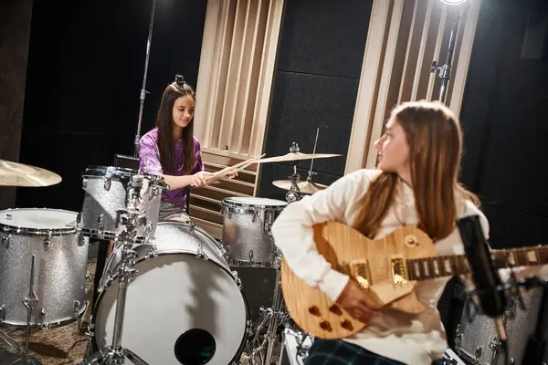 Foco na menina adolescente morena bonita tocando bateria ao lado de seu amigo borrado tocando guitarra — Fotografia de Stock