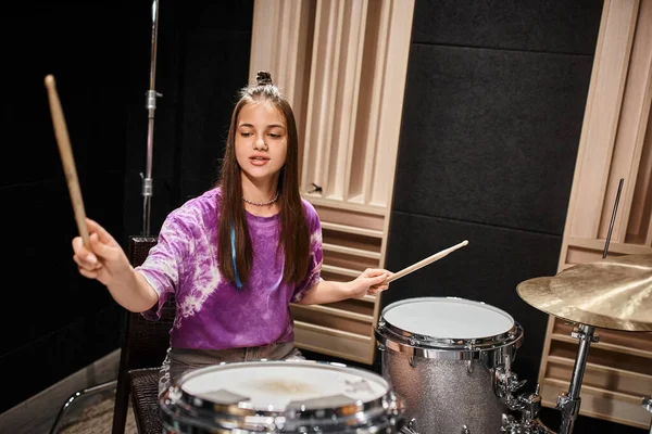 Gut aussehende stilvolle Teenager-Mädchen in lässiger, lebendiger Kleidung, die ihr Schlagzeug spielt, während sie im Musikstudio ist — Stockfoto