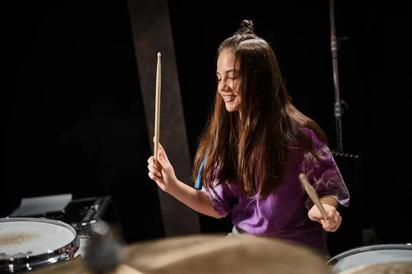 Gioiosa bella ragazza adolescente bruna di talento con i capelli lunghi che suona la batteria in studio — Foto stock