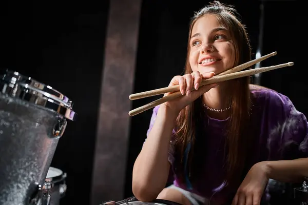 Jolly brunette teenage girl in everyday vivid attire posing with drumsticks and looking away — Stock Photo