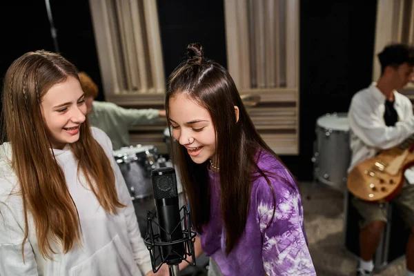 Alegres adoráveis adolescentes cantando em microfone e menino tocando instrumentos em estúdio — Fotografia de Stock