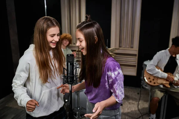 Meninas adolescentes bonitas cantando no microfone enquanto meninos tocando bateria e guitarra, grupo musical — Fotografia de Stock