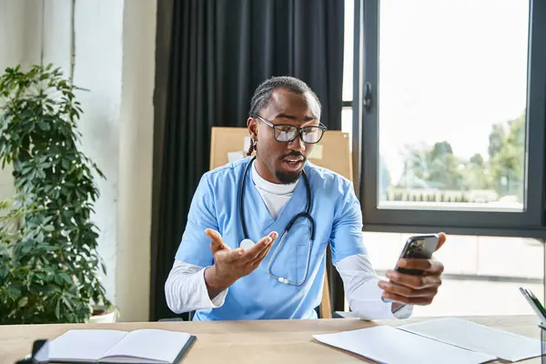 Jeune médecin afro-américain avec des lunettes consulter quelqu'un par téléphone portable, télémédecine — Photo de stock
