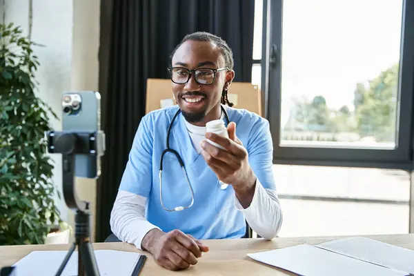 Joyeux jeune médecin afro-américain avec des lunettes montrant des pilules à la caméra de téléphone mobile, télémédecine — Photo de stock