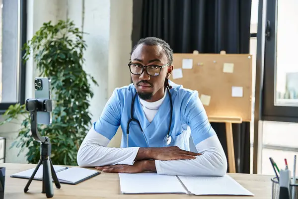 Handsome focused african american doctor with glasses looking at camera during online consultation — Stock Photo