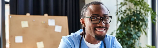 Радісний афроамериканський лікар в окулярах дивиться на камеру під час онлайн-консультації, банер — стокове фото
