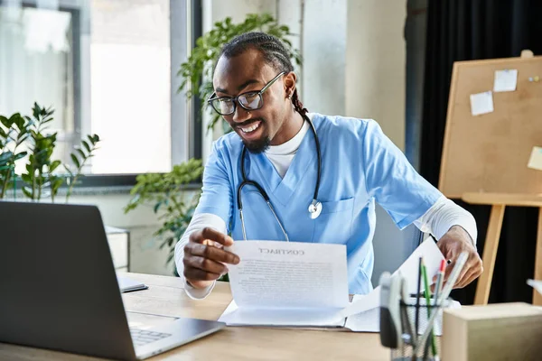 Красивый веселый африканский американский врач держит свои заметки во время онлайн-консультации, телездравоохранения — стоковое фото