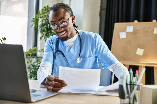 Привабливий радісний афроамериканський лікар тримає нотатки під час онлайн-консультації, телемедицина — стокове фото