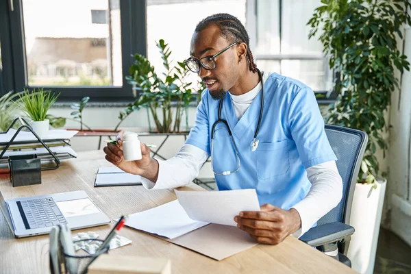 Souriant médecin afro-américain tenant des notes et des pilules lors de la consultation en ligne, la télémédecine — Photo de stock
