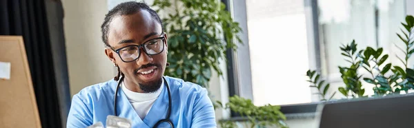 Веселый африканский американский врач с таблетками в руке, глядя на камеру ноутбука, телемедицину, баннер — стоковое фото