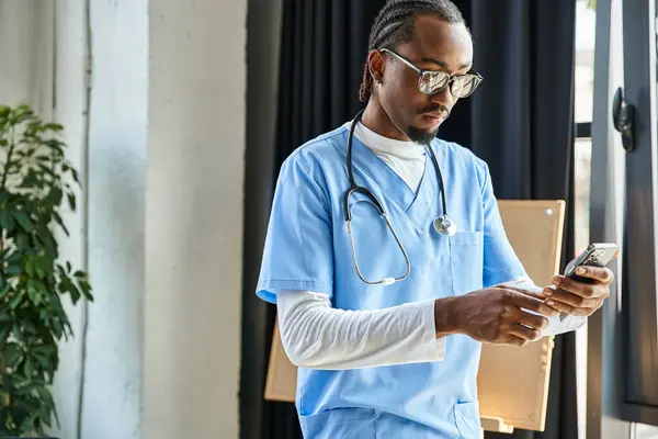 Bonito pensativo Africano americano médico com estetoscópio olhando para o seu telefone celular, telemedicina — Fotografia de Stock