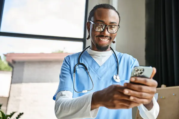 Bonito alegre Africano americano médico com estetoscópio olhando para o seu telefone celular, telemedicina — Fotografia de Stock