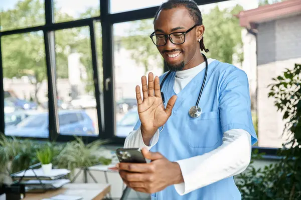 Alegre jovem médico afro-americano com estetoscópio acenando em seu telefone celular, telemedicina — Fotografia de Stock