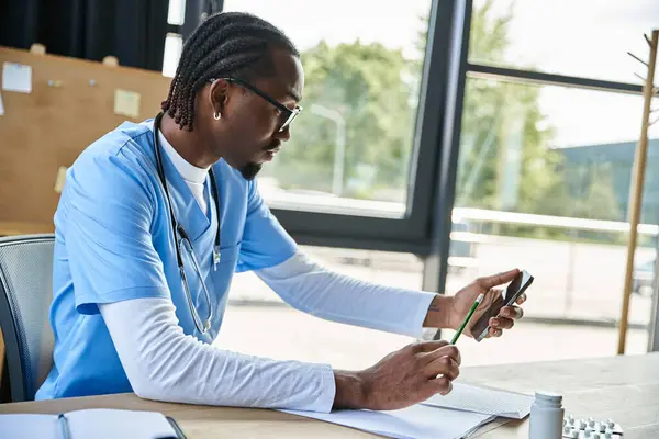 Médecin afro-américain concentré avec des lunettes prendre des notes et de consultation par téléphone, la télésanté — Photo de stock