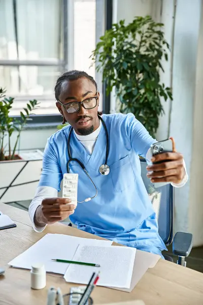 Концентрированный африканский американский врач консультирует пациента по телефону и держит таблетки, телемедицина — стоковое фото