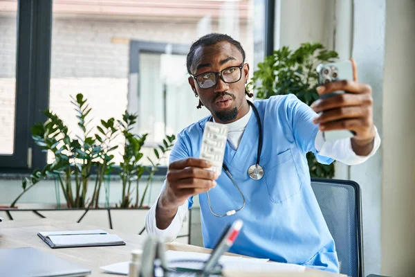 Médecin afro-américain onéreux consultant patient par téléphone et tenant des pilules, télémédecine — Photo de stock