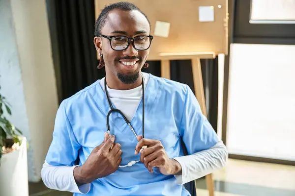Joyeux jeune médecin afro-américain avec stéthoscope et lunettes souriantes et regardant la caméra — Photo de stock
