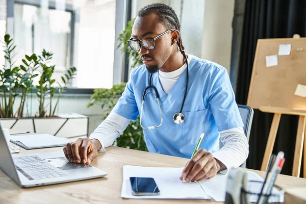 Focused good looking african american doctor with glasses taking notes attentively while at office — Stock Photo