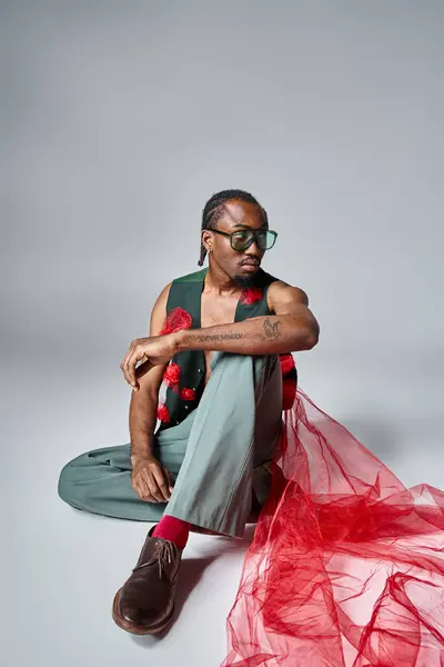 Schöner afrikanisch-amerikanischer Mann mit rotem Tüll auf der Weste auf dem Boden sitzend, Modekonzept — Stockfoto