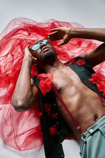 Привабливий модний афроамериканський чоловік з сонцезахисними окулярами у яскравому вбранні, лежачи на підлозі, мода — стокове фото